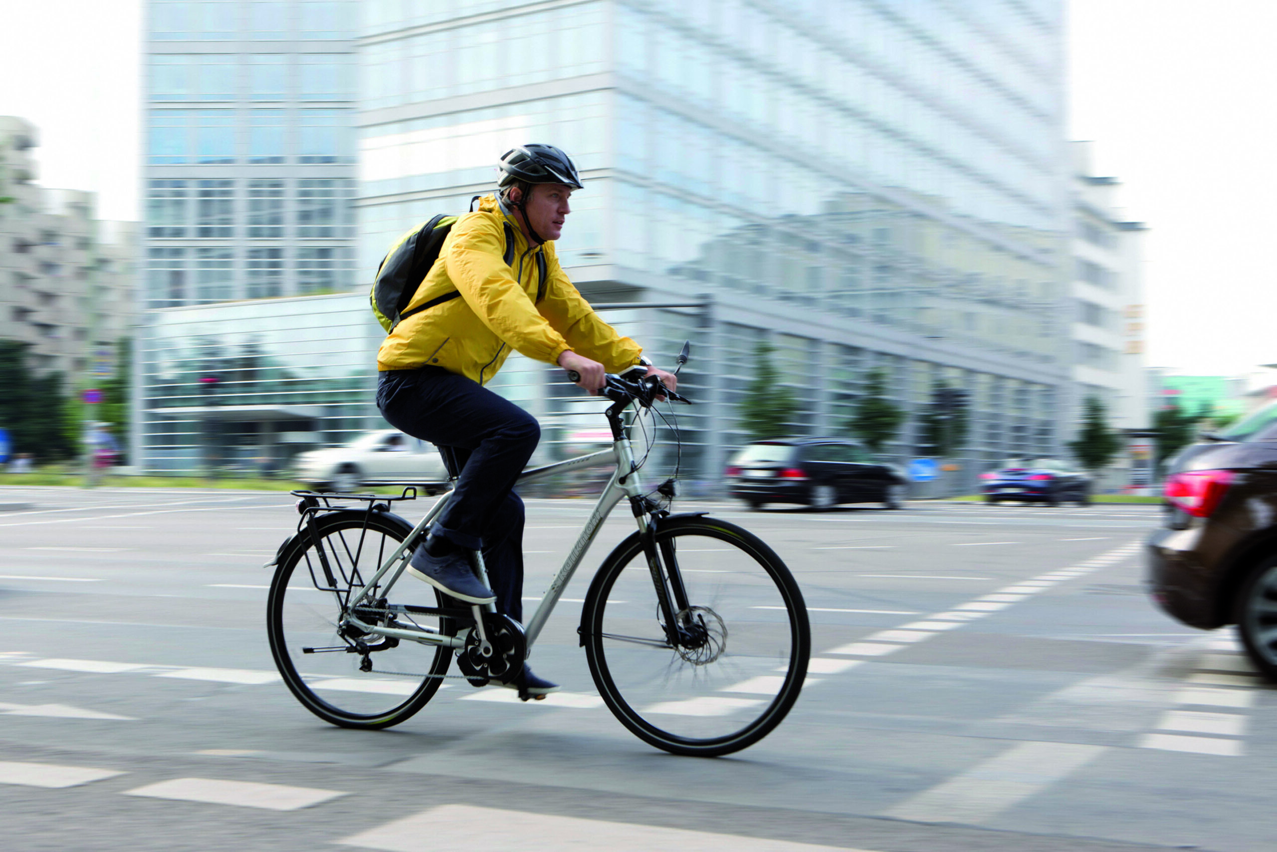 Radfahrer mit gelber Jacke und Rucksack fährt durch den Stadtverkehr.