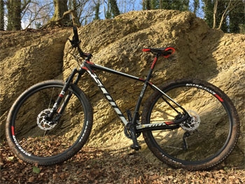 Scott Scale 950 Mountainbike vor Felswand im Wald, ideal für Offroad-Abenteuer und Geländetests.
