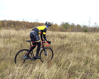 Radfahrer fährt mit dem Focus Mares AL 105 Cyclocross-Bike in Seitenansicht über bewachsenes Gelände.