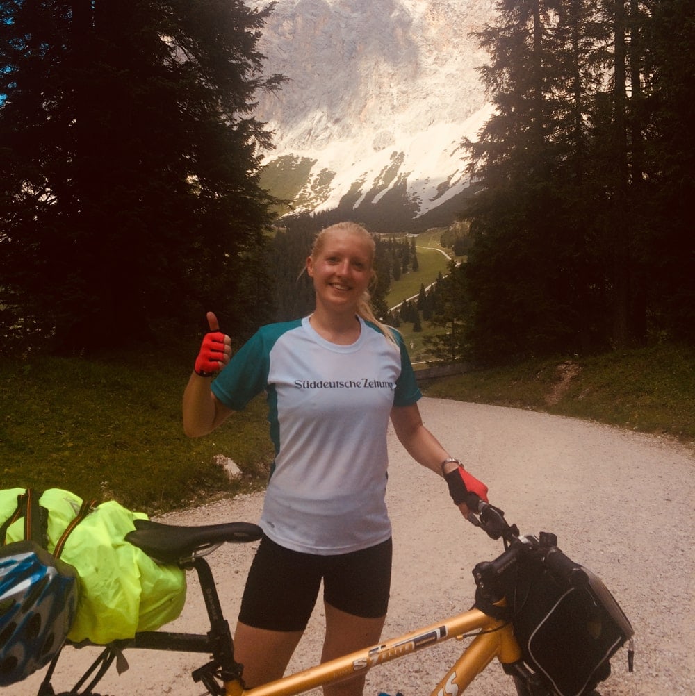 Frau in Sportbekleidung steht neben ihrem Fahrrad und zeigt Daumen hoch