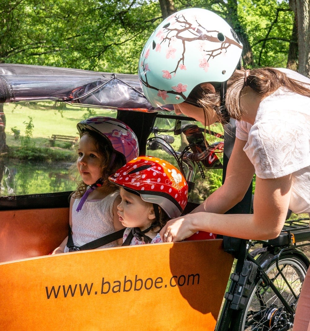 Testerin Nicola beugt sich zu zwei Kindern mit Fahrradhelmen in der Transportbox eines Babboe Lastenrads.