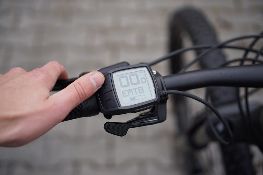 Nahaufnahme des Bosch Purion E-Bike-Displays am Lenker, das mit der Hand bedient wird.
