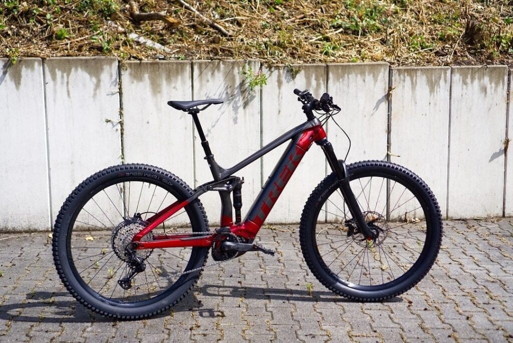 Rot-schwarzes Trek Rail 7 E-Mountainbike in Seitenansicht vor einer Betonwand.