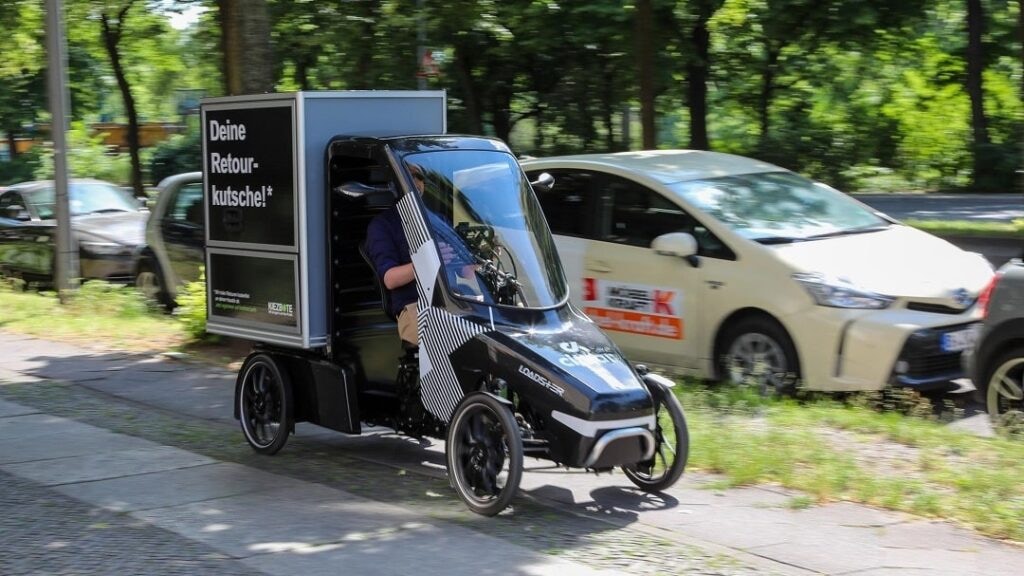 Mann fährt mit einem Citkar Loadster Lastenrad mit der Aufschrift "Deine Retourkutsche" auf einem Fahrradweg.