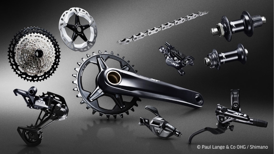 Darstellung der einzelnen Komponenten einer Shimano XT M8100 Mountainbike-Schaltgruppe mit Schaltwerk, Kassette, Kette und Kurbel.