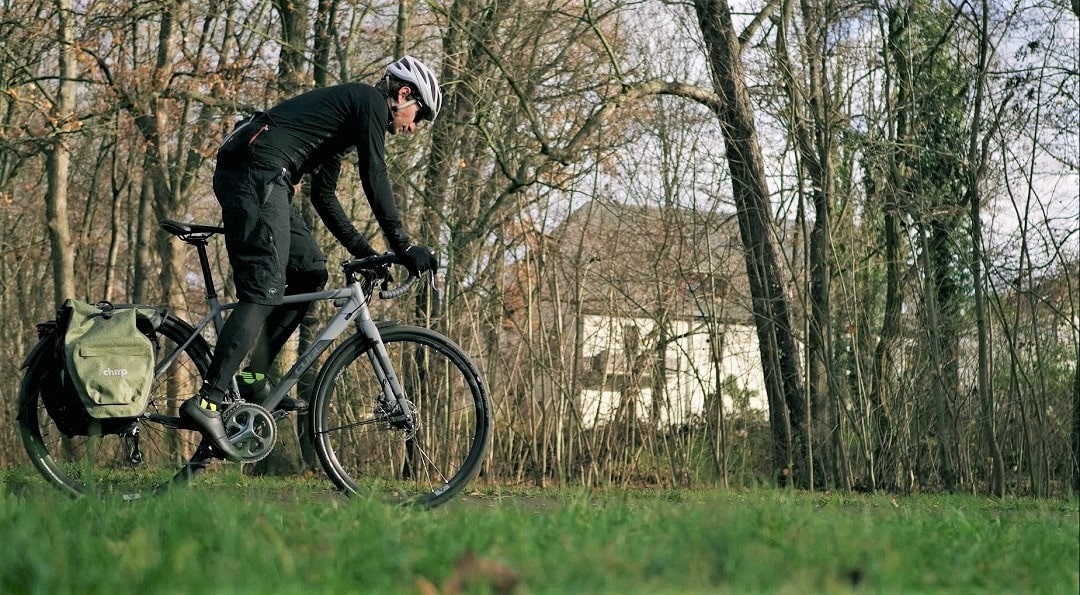 Fahrradfahrer auf dem Cube Nuroad Pro FE Gravelbike in Seitenansicht mit kompletter Alltagsausstattung fährt über eine Wiese.