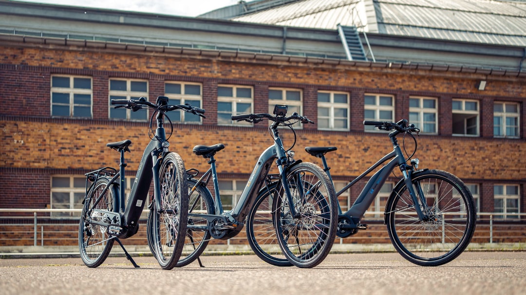 Drei moderne E-Bikes der 2R Manufaktur ELX-Serie vor einem Backsteingebäude.