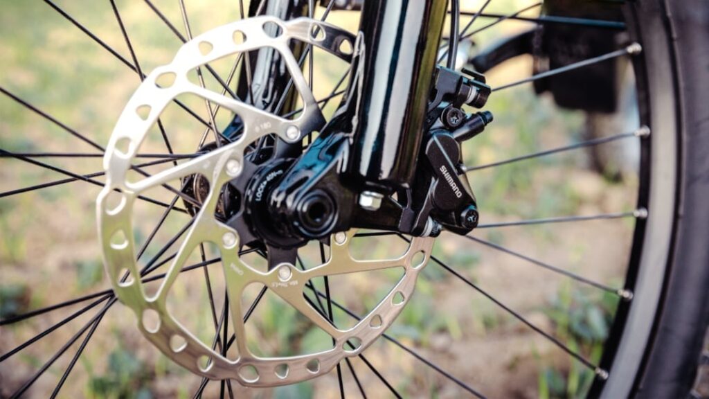 Scheibenbremse eines E-Bikes, Nahaufnahme, zeigt Details der Bremsanlage und Speichen im Hintergrund.