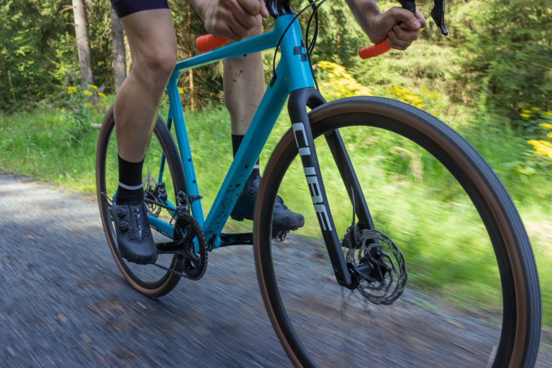 Nahaufnahme eines blauen Cube Cross Race Pro Cyclocrossrads mit Fahrer auf einem Schotterweg.