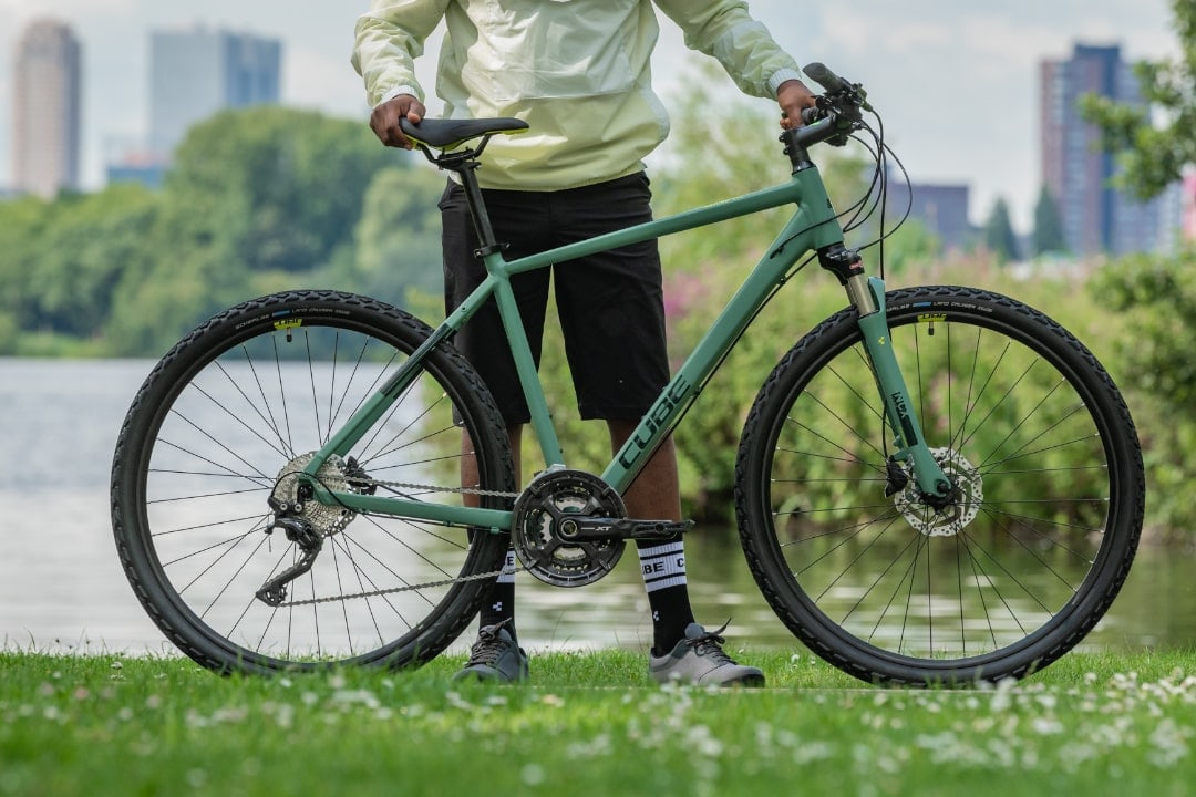 Cube Nature EXC Crossbike mit Federgabel und Scheibenbremsen vor einem See und städtischer Kulisse.