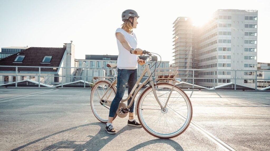Radfahrerin mit Citybike und Helm vor urbaner Kulisse.