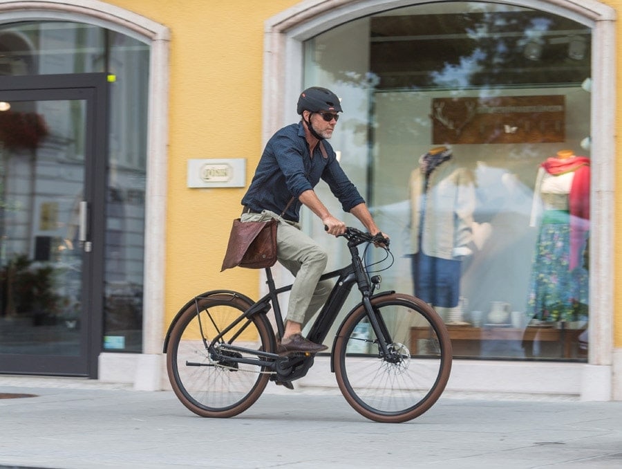 Radfahrer mit Helm und Umhängetasche fährt mit dem E-Bike durch die Stadt.