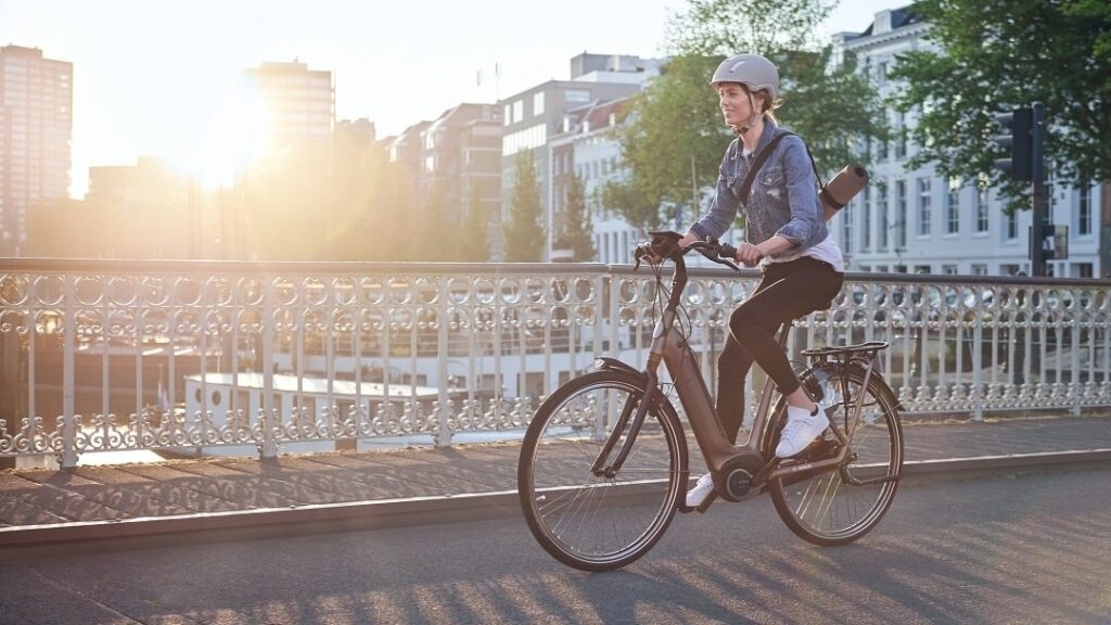 Radfahrerin mit Helm und Rucksack fährt mit dem E-Bike über eine Brücke in der Stadt.