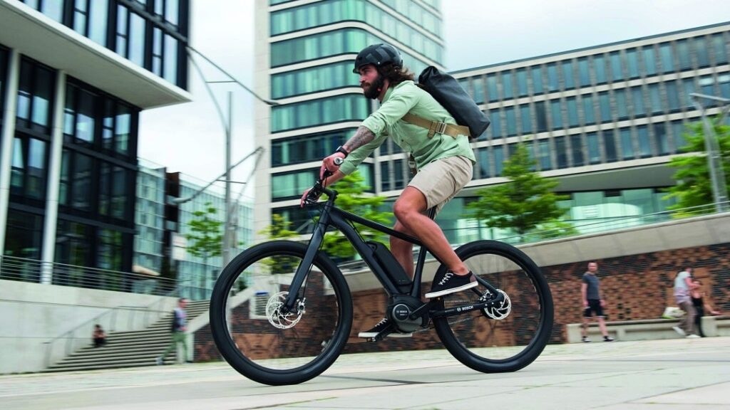 Pendler fährt mit E-Bike und Rucksack durch die Stadt.