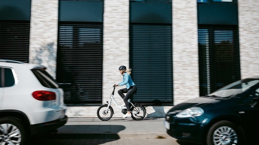 Radfahrerin fährt mit einem Faltrad zwischen Autos durch die Stadt.
