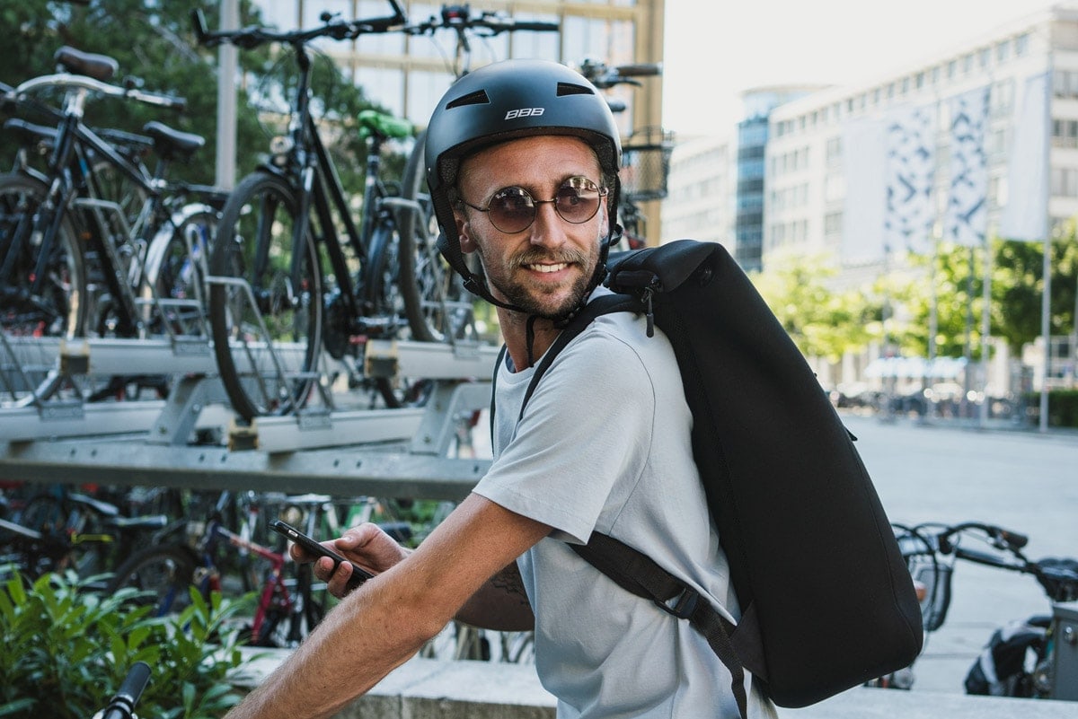 Radfahrer mit Cityhelm, Sonnenbrille und Rucksack in städtischer Umgebung.
