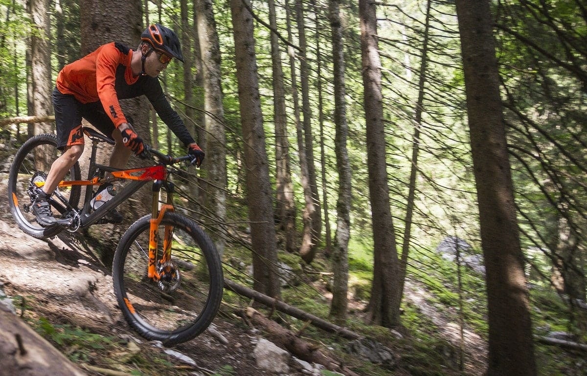Mountainbiker mit Helm fährt auf einem Waldweg bergab.
