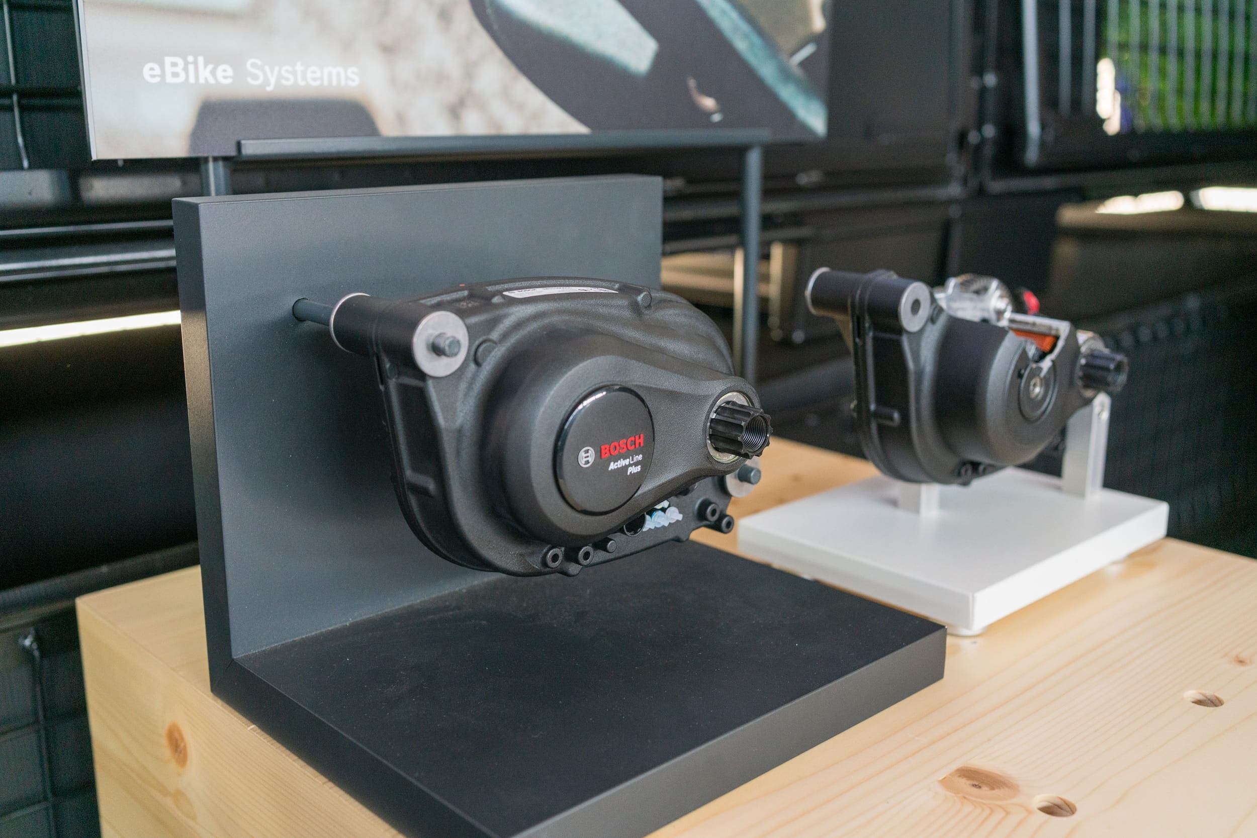 Zwei Bosch Active Line Plus Antriebseinheiten auf Präsentationsständern, ausgestellt auf einem Holztisch vor einem Bosch eBike Systems Hintergrund.