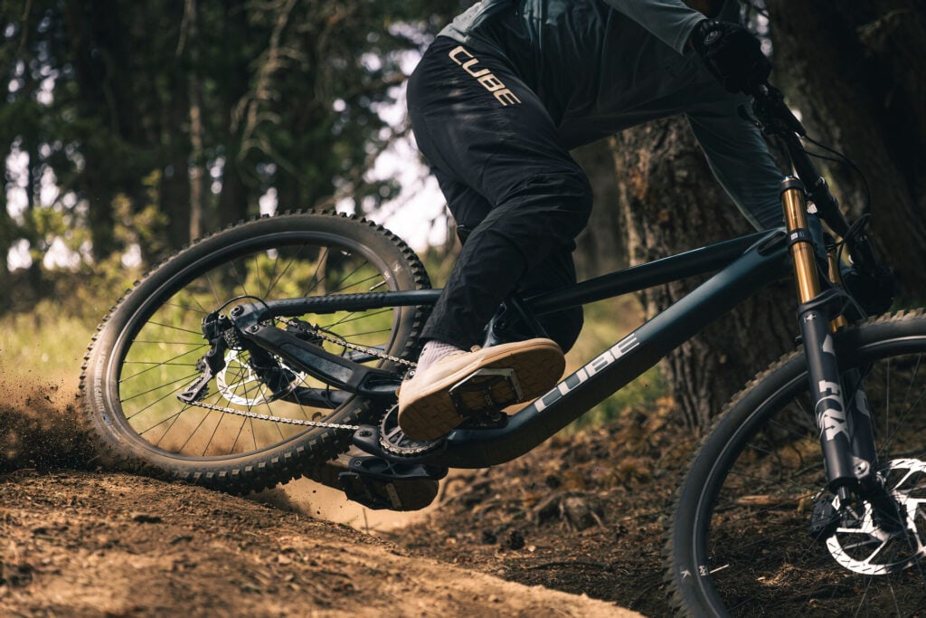 Eine Person fährt mit einem Mountainbike eine Piste entlang und wirbelt dabei mit dem Hinterrad sehr viel Dreck auf