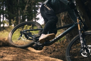 Eine Person fährt mit einem Mountainbike eine Piste entlang und wirbelt dabei mit dem Hinterrad sehr viel Dreck auf